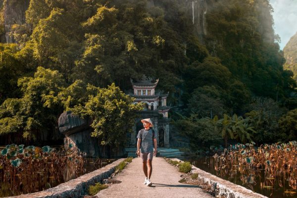 Traveler walking along a stone path toward the ancient gate of Bich Dong Pagoda in Ninh Binh Vietnam