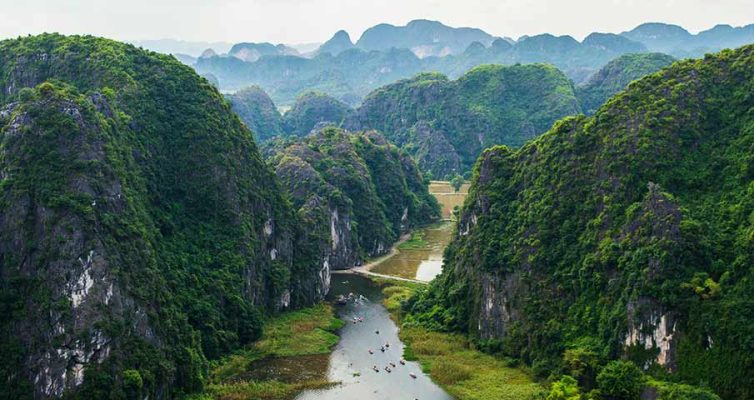 Tam Coc river with boats sailing between limestone mountains and green rice fields in Ninh Binh, Vietnam