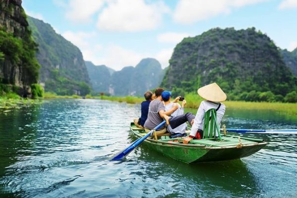 Tourists on a small sampan boat in Tam Coc, Ninh Binh, rowing through limestone mountains and lush rice fields